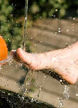Eine Person spült ihren Fuß unter einem Wasserstrahl ab, wobei Wassertropfen umherspritzen.