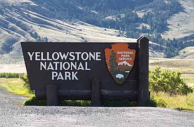 Holzschild mit der Aufschrift „Yellowstone-Nationalpark“ am Eingang des Parks, mit einer Berglandschaft im Hintergrund.